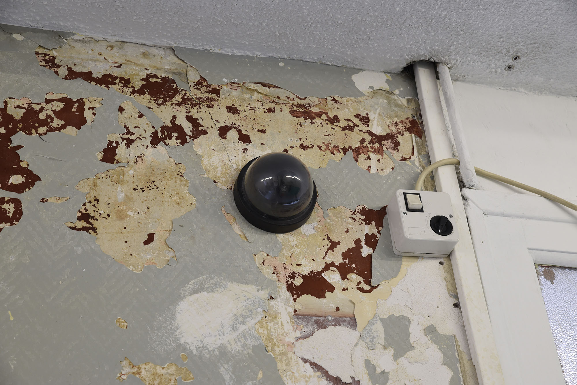 Sur un mur décrépi, une caméra de surveillance en forme de demi-globe est posée.